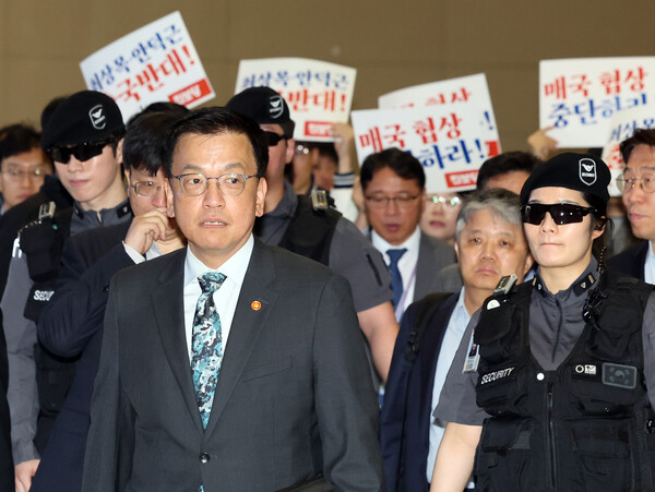 최상목 부총리 겸 기획재정부 장관이 22일 오전 인천국제공항에서 한미 2+2 통상협의 참석을 위해 출국하고 있다. 출국하는 최 부총리 뒤쪽으로 진보당원들이 손팻말을 들고 대미 협상 추진을 규탄하고 있다. (사진=뉴스1)